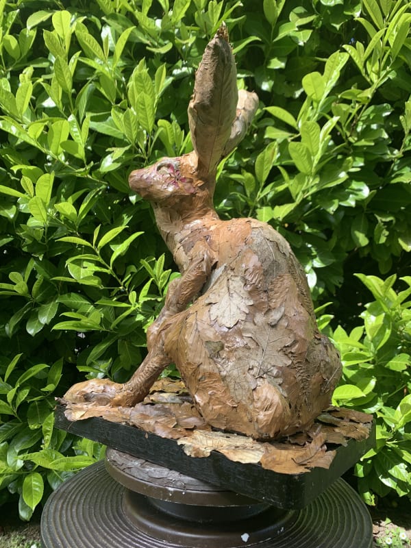 Sitting leafy hare garden sculpture against a green hedge