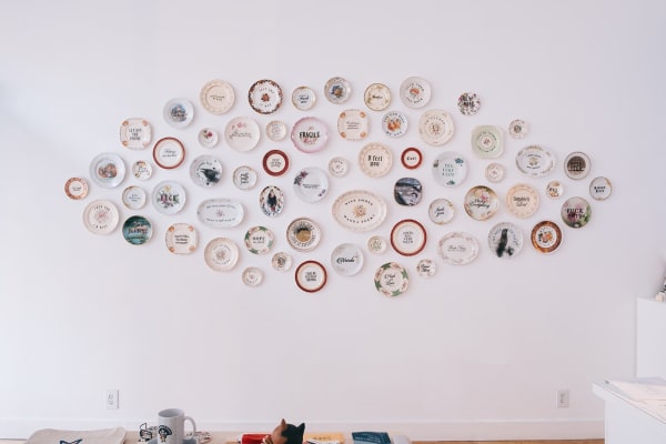 Install shot of decorative plates hung in an oval arrangement on a wall as part of MC Marquis exhibition