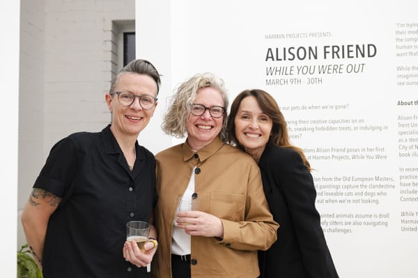 Alison Friend with her friends in front of the wall text for her solo exhibition "While You Were Out..."