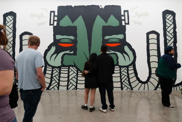 A couple standing close together in front of a large GATS mural at Hashimoto Contemporary Los Angeles