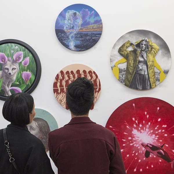 Photo of a man and a woman looking at circular paintings hanging on a white wall 