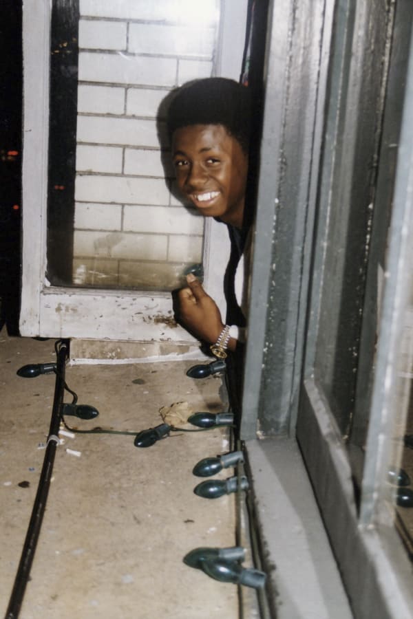 A photo by Polo Silk of a 15-year-old Lil Wayne smiling, poking his head out of a window at the New Orleans House of Blues.