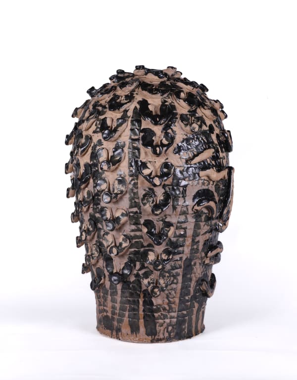 Earth toned low relief sculpture in the shape of a head with dark glazed coils and markings.