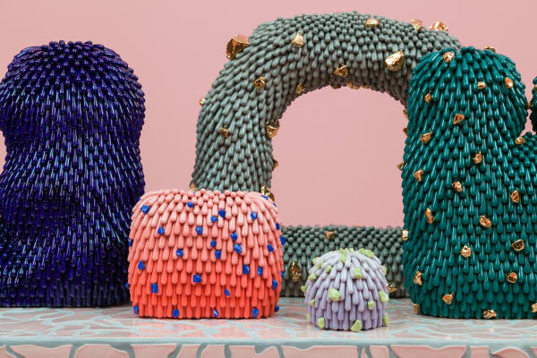 Installation shot of somebody with a detail of the Furries. From left to right: "Space Denim Dust Furry," "Mango Dust Furry with Blue Rocks," "Astroid Warbler Dust Furry," "Purple Dust Furry with Neon Rocks,", and "Nebula Furry with Gold Rocks."