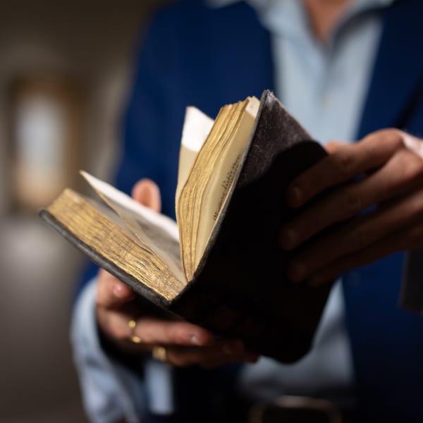 Close-up of a person in a blue suit holding and flipping through a richly illuminated Book of Hours from the late Middle Ages, with golden page edges.