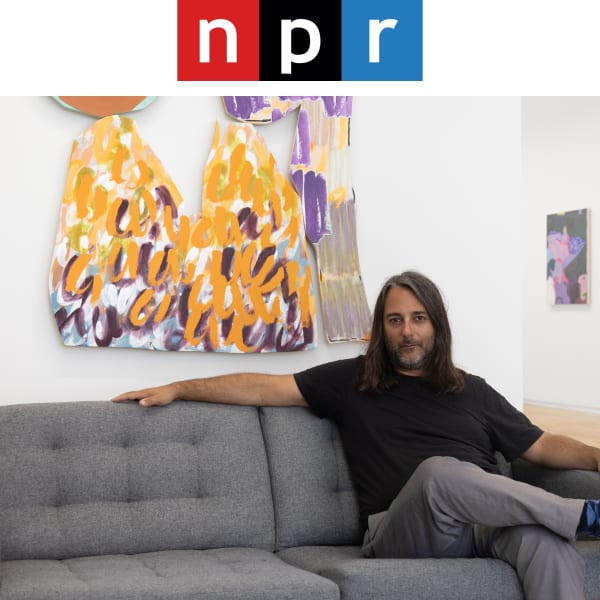 Top is a logo with the letters “n” on a red square, “p” on a black square, and “r” on a blue square with the photos of a man with shoulder length dark hair, scruff, a black tee and grey slacks, sits on a mid-modern grey couch in front of a white room with