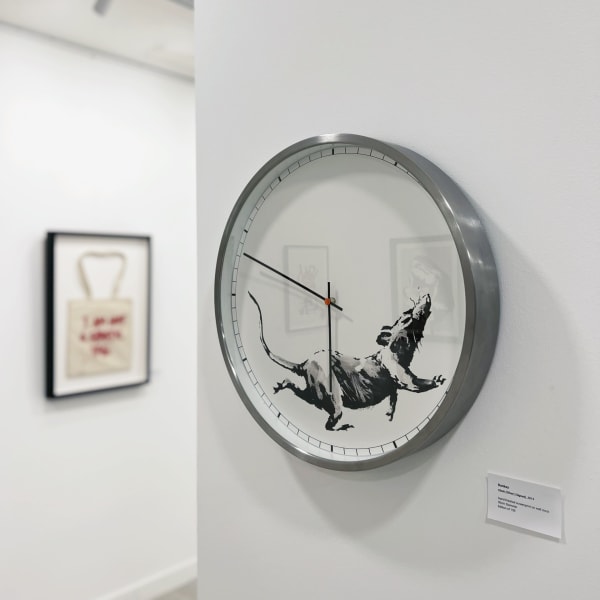 Clock artwork by Banksy featuring a rat design on a wall in an art gallery setting