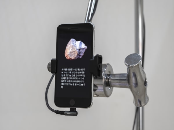 Detail: Daisy-Chain-Agora, 2023, iPhone, steel stand, grip head with arm, charger, cable, adhesive PVC sheet, dimensions variable, 5-channel video, 27min(loop), color, sound, AI model(GPT-4, Stable Diffusion), Curtesy Hong Cheol Gi
