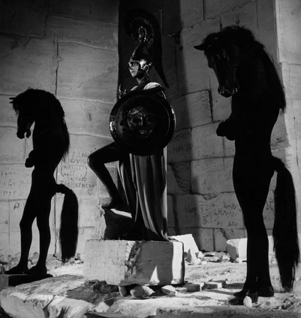 Black and white photograph of Jean Cocteau in costume standing between two humanoid horse figures