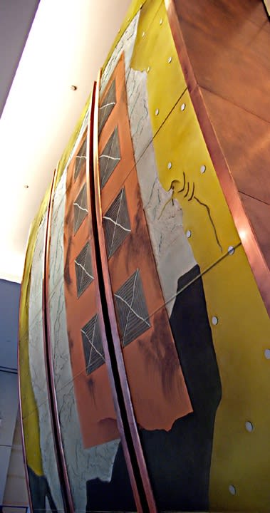 Large curved sculpture of dichroic glass by Warren Carther rising from the wall with brass, steel grey, and green colors