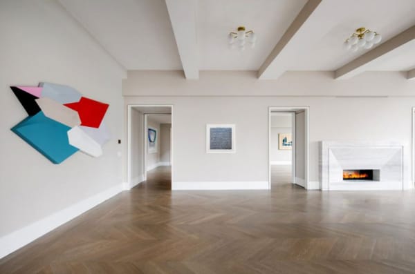 An interior room painted in light beige with dark wood herringbone flooring. Artwork hangs on the walls.