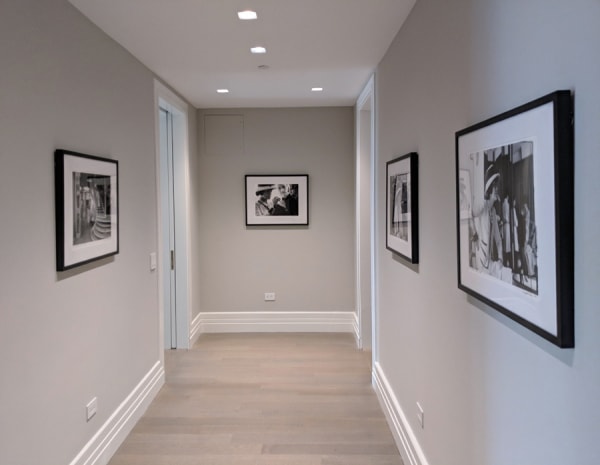 An interior room painted in light beige with dark wood herringbone flooring. Photography of Coco Chanel hangs on the walls.