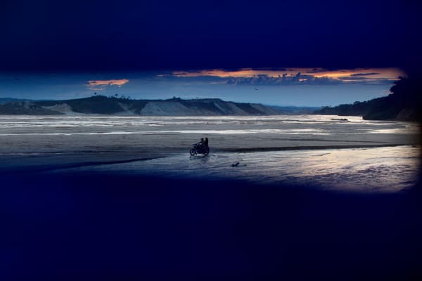 Two persons riding a motorcycle through a wasteland created by illegal gold mining near Huepethaue