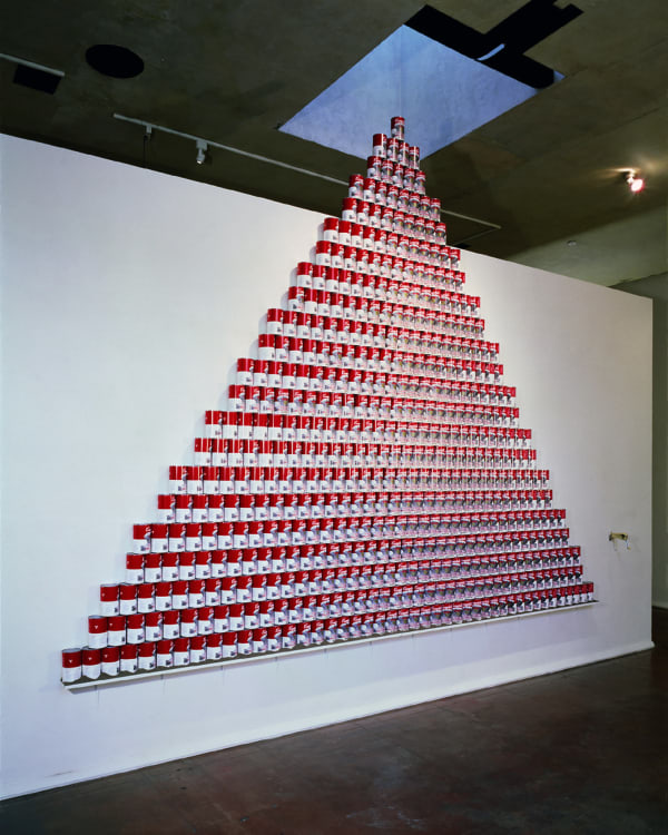 An array of red and white soup cans by artist Nobuho Nagasawa in a pyramid formation on a gallery wall