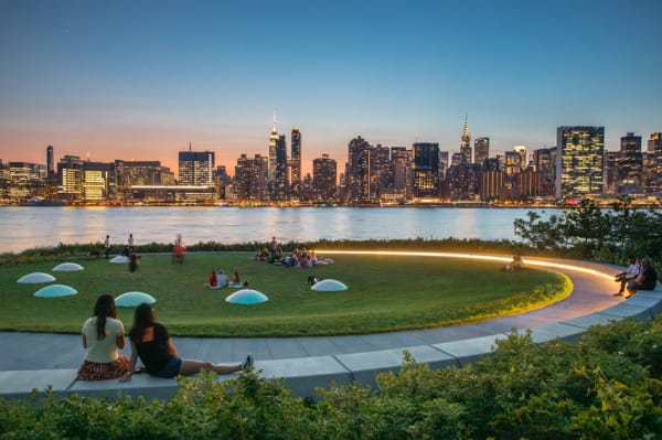 Detail with city view of a Public park with circular moon sculptures placed in a semicircle on a green lawn, next to a bay