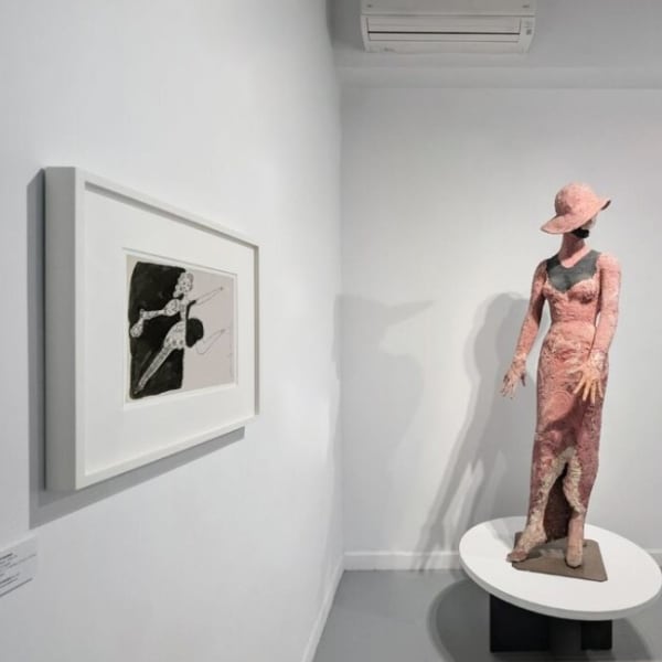 A mannequin in a sculpted coral dress and a drawing of a dancer by Andy Warhol on adjacent walls of a gallery