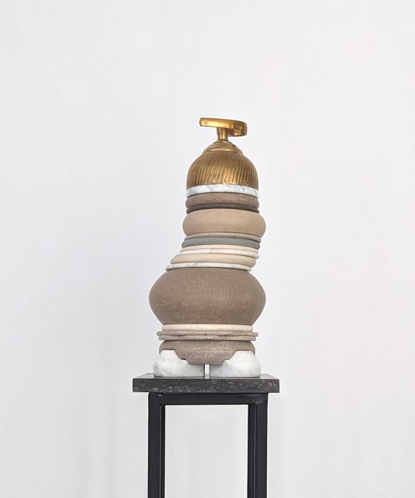 Stacked stone sculpture with brass cap rests atop a thin steel pedestal