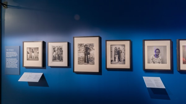 Black and white photographs in black frames hanging on a blue wall in a museum like setting