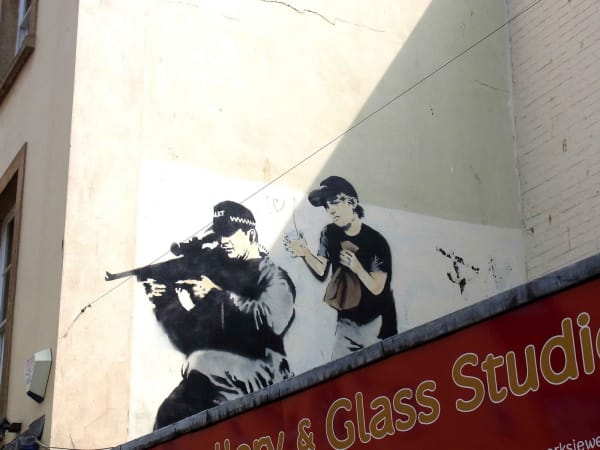Banksy’s 2011 Police Sniper and Paper Bag Boy street scene fuses tension and playful misdirection.