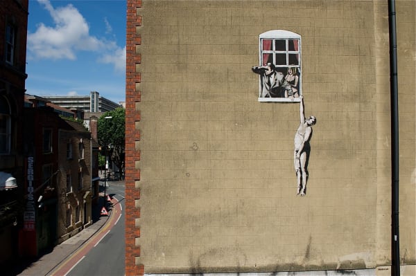 Banksy’s 2006 Naked Man Hanging From Window mural adds playful humour to an urban street facade.