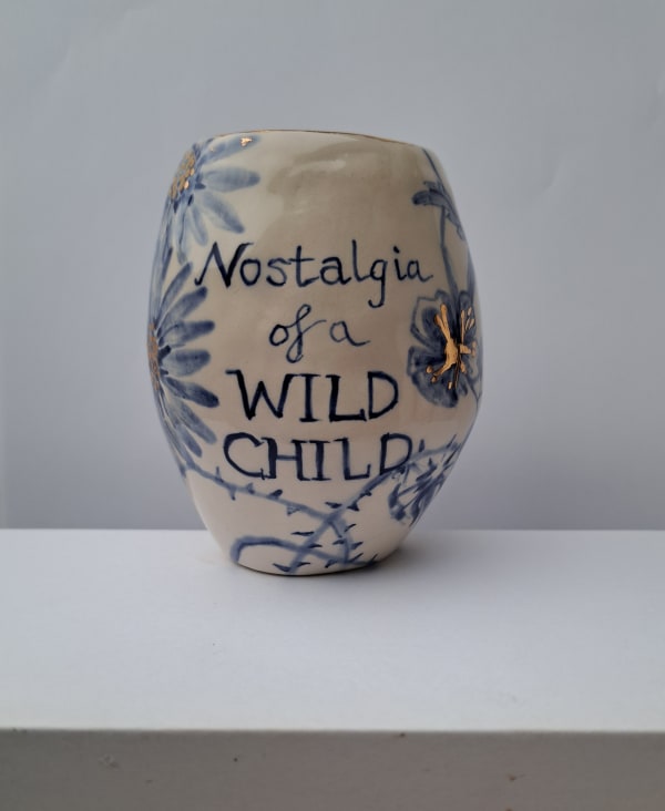 Ceramic vase with blue floral designs and text 'Nostalgia of a Wild Child' on a white background.