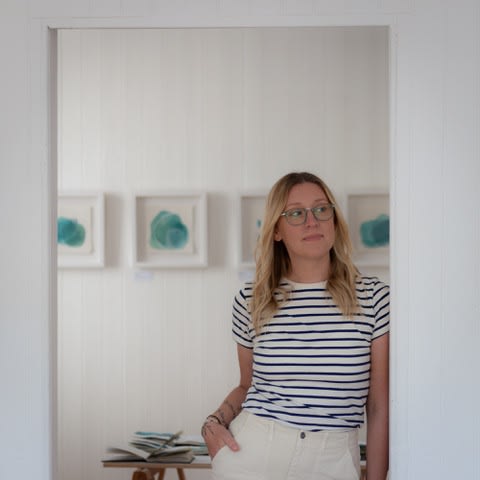 Jane Hunter in a striped shirt standing in an art gallery with abstract paintings in the background.