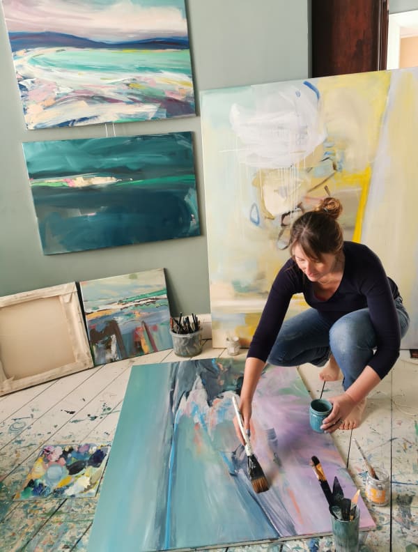 Artist Mary McDonald working in her studio surrounded by colourful abstract paintings.