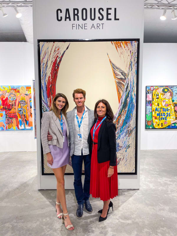 People posing in front of paintings displayed at Carousel Fine Art's booth at the art fair, Context Art Miami 2021.