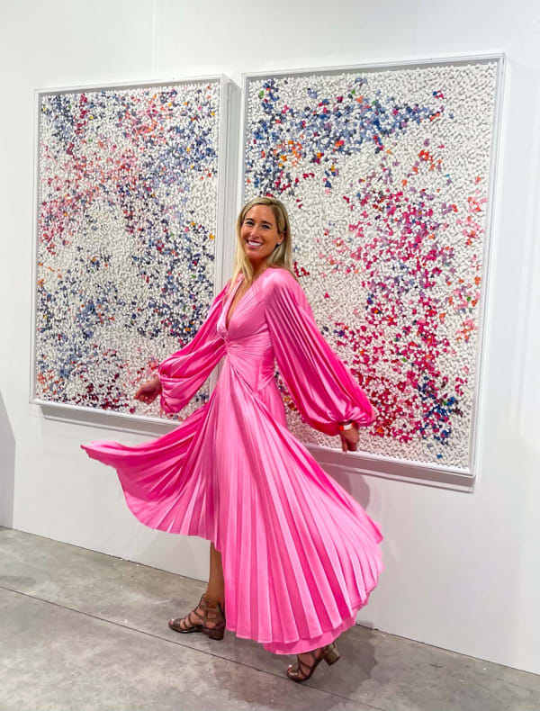Woman posing in front of paintings displayed at Carousel Fine Art's booth at the art fair, Context Art Miami 2021.