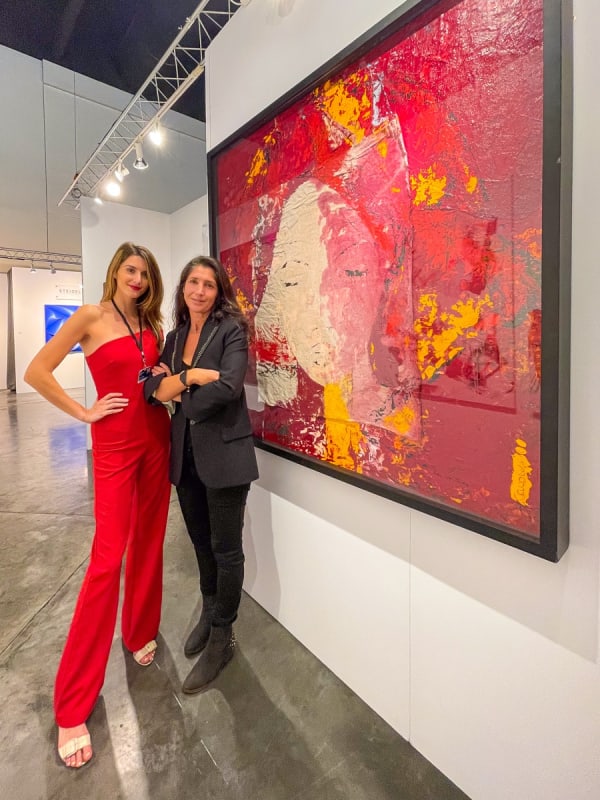 Women posing in front of paintings displayed at Carousel Fine Art's booth at the Palm Beach Show art fair, 2022.