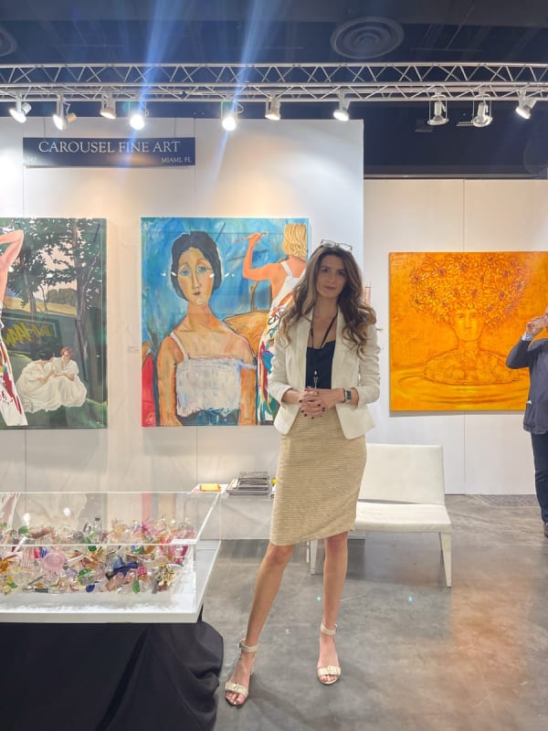 Woman in front of paintings displayed at Carousel Fine Art's booth at the Palm Beach Show art fair, 2023.