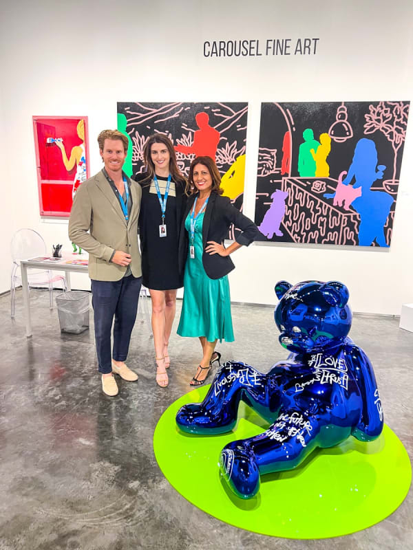 Owners of Carousel Fine Art posing at their gallery booth at the Palm Beach Modern and Contemporary art fair, 2023, surrounded by paintings and sculpture.