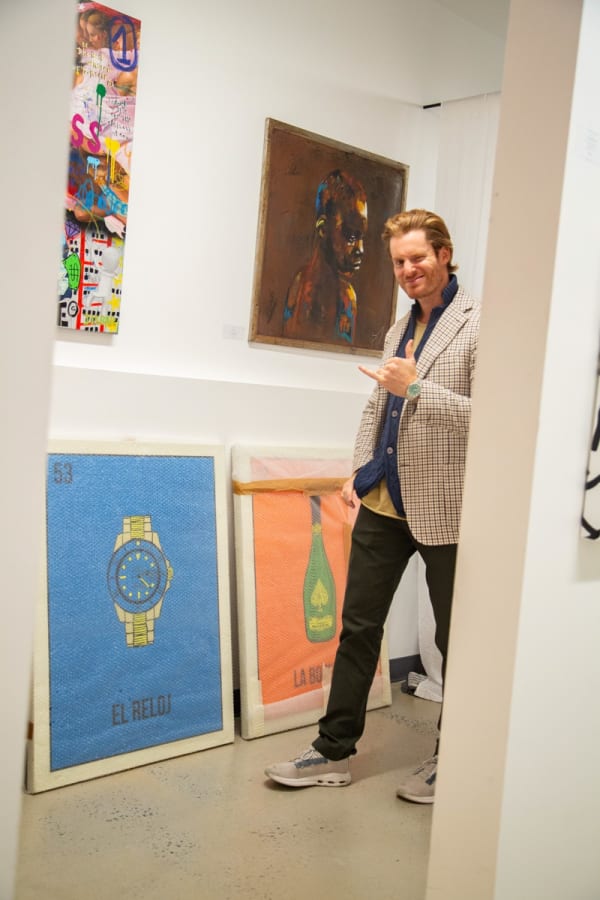 Man surrounded by paintings propped against the wall on the floor in a storage space.
