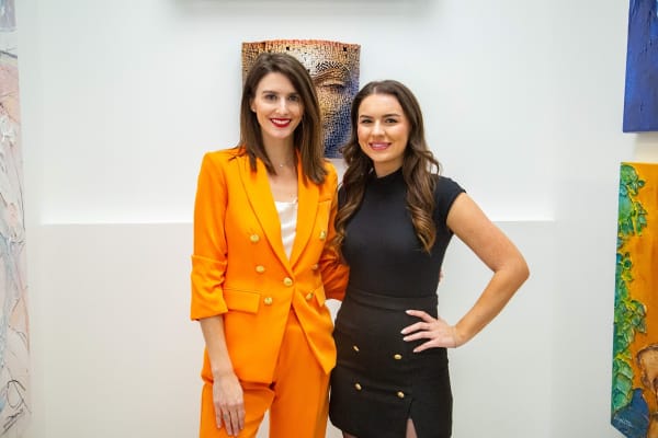 Women posing in front of paintings displayed at Carousel Fine Art's new gallery space in Buckhead Village, Atlanta during an event for their grand opening.