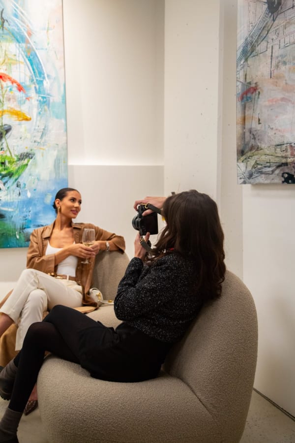 A woman taking a photo of another woman on a couch at Carousel Fine Art's new gallery space in Buckhead Village, Atlanta during an event for their grand opening.