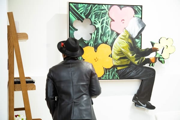 Man staring at Hijack's painting "They Love Me, They Love Me Not," hanging on a wall.