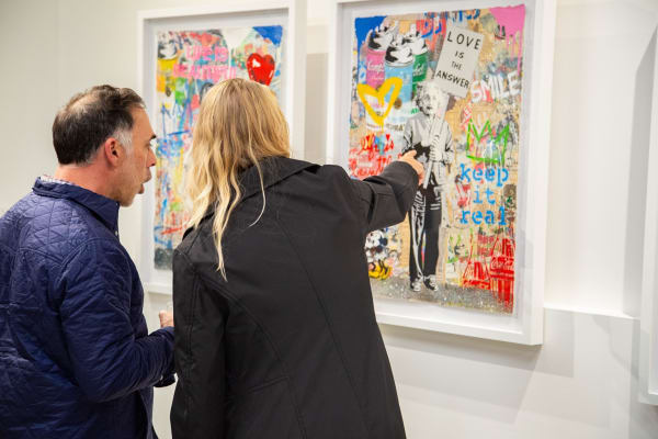 People pointing at paintings displayed at Carousel Fine Art's new gallery space in Buckhead Village, Atlanta during an event for their grand opening.