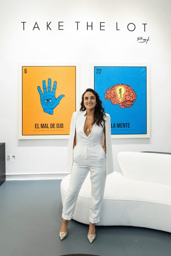 Artist, Cayla Birk posing in front of her artworks displayed in Carousel Fine Art's Miami location for the Cayla Birk exhibition, "It's in the Cards."
