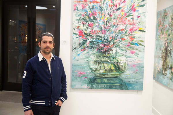 Artist Eric Alfaro posing in front of his paintings displayed in Carousel Fine Art's Buckhead Village location during the Eric Alfaro exhibition "Spring Reverie."