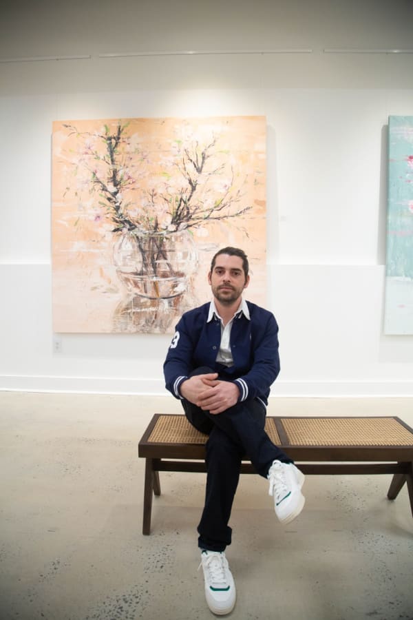 Artist Eric Alfaro posing in front of his paintings displayed in Carousel Fine Art's Buckhead Village location during the Eric Alfaro exhibition "Spring Reverie."