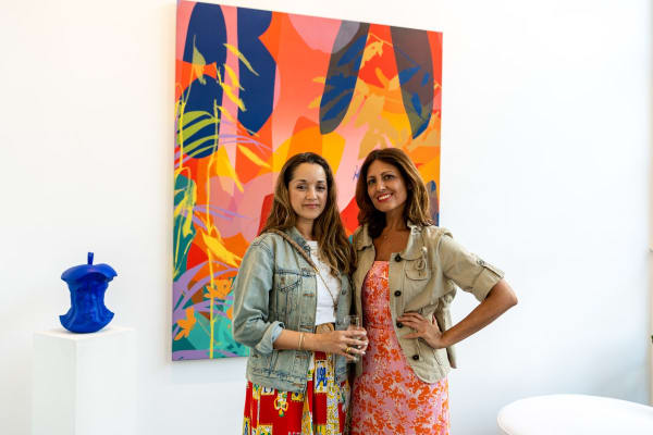 People posing in front of paintings displayed in Carousel Fine Art's Miami gallery space during Neill Wright's exhibition "Where the Light Gets In."
