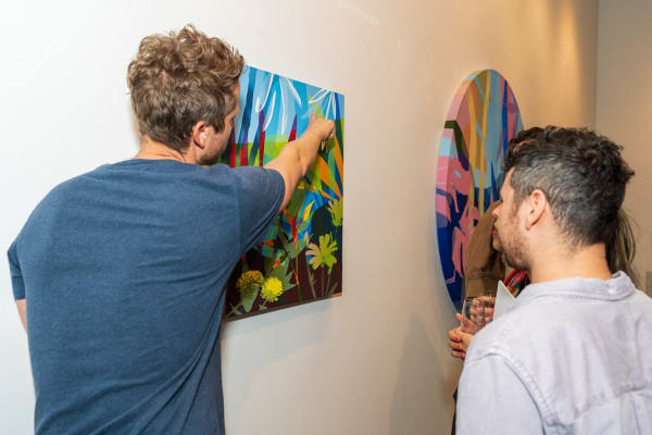 Artist Neill Wright pointing at his paintings displayed in Carousel Fine Art's Miami gallery space during Neill Wright's exhibition "Where the Light Gets In."