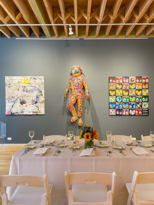 Table decorated for Collector's Dinner at Carousel Fine Art's gallery space in Chicago with paintings and sculpture hung on wall.
