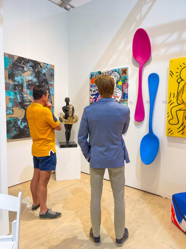 Men staring at paintings and sculptures displayed at Carousel Fine Art's gallery both at the Hampton's Art Market, 2021.