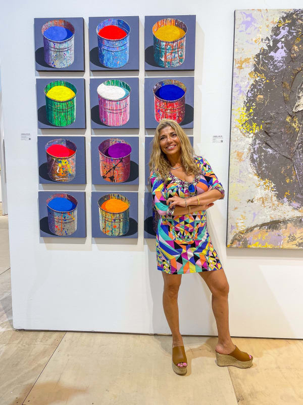 Woman posing in front of paintings displayed at Carousel Fine Art's booth at the Palm Beach Show art fair, 2022.