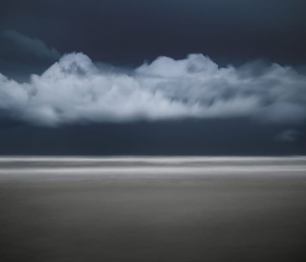 horizon line of still water with white cloud along horizon line with dark sky behind.