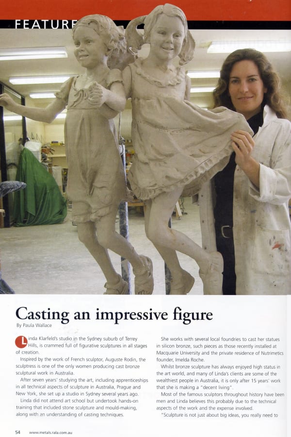 Linda Klarfeld stands in her Terrey Hills studio beside two life-sized clay sculptures of young girls holding hands and smiling, part of her figurative work. The sculptures are shown in progress, with a detailed focus on their playful expressions and flow