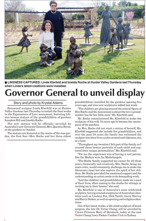 Linda Klarfeld and Imelda Roche are pictured together at Hunter Valley Gardens, surrounded by bronze statues of children from the Expressions of Love monument. Linda kneels beside a sculpture of a child, while Imelda stands behind her, smiling. The sculpt