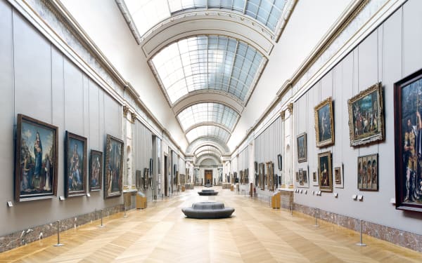 Photograph by Candida Hofer showing the interior of the Louvre museum - a large light filled gallery with paintings on the walls, wooden floor and a glass roof