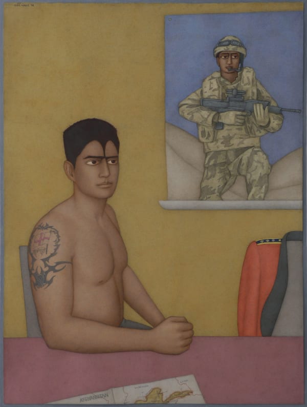 A shirtless off duty Marine sits in his home on a chair, a picture of him in his uniform is hung on the wall behind him